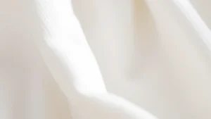 Close-up of soft organic cotton fabric texture with gentle natural lighting, showing the delicate weave suitable for baby clothing