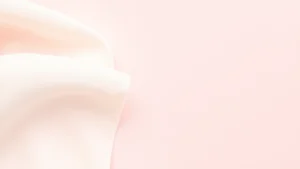 Close-up of soft organic cotton fabric texture against a pale pink background, showing natural fibers and weave detail, gentle and delicate