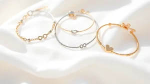 Close-up of delicate baby bracelets and anklets displayed on soft white fabric, showing various metal finishes and closure types in natural lighting