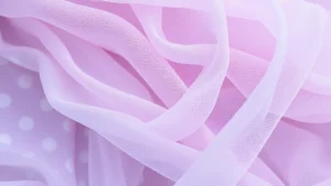 A close-up of flowing iridescent and tulle fabrics in soft lavender, silver, and pearl tones layered together, showing texture and movement